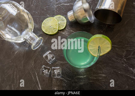 Piatto di laici vintage gin succhiello cocktail guarnito con calce fresca fetta, bottiglia di gin, shaker con cubetti di ghiaccio su nero . Foto Stock