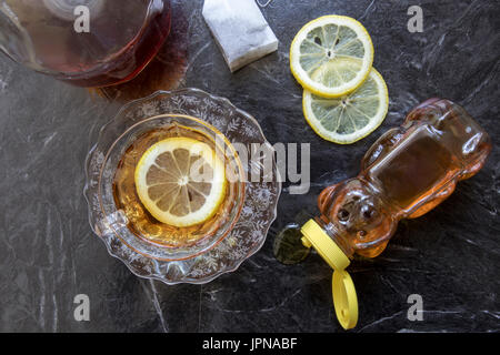 Tazza classica di hot toddy cocktail in coppa di cristallo e il piattino con il miele, le fette di limone e un sacchetto da tè nero. Foto Stock