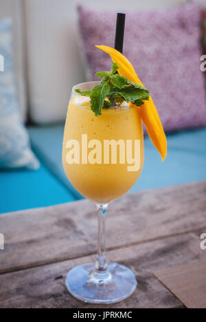 Frullato di succosa da mango in vetro con paglia e menta decorazione su un tavolo di legno. La vita sana. Foto Stock