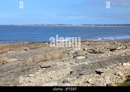 Guardando sulla baia verso Porthcawl e il suo promontorio, è a suo modo con spruzzi delle onde contro le rocce su una tranquilla e soleggiata giornata. Foto Stock