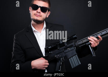 Giovani gangster utilizzando la sua arma a cantare su di esso cercando rilassato su sfondo nero Foto Stock