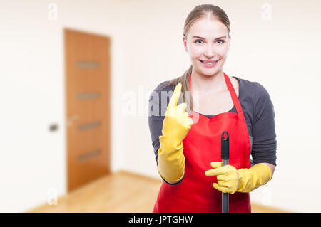 Giovane attraente casalinga rising un dito di una mano mentre si esegue la pulizia con lo spazio di testo Foto Stock