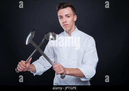 Giovane maschio cook con utensili da cucina isolati su sfondo nero Foto Stock