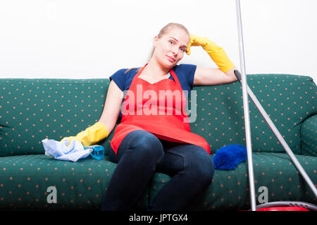 Lazy giovane donna appoggiata sul divano durante la pulizia e prendendo una pausa Foto Stock