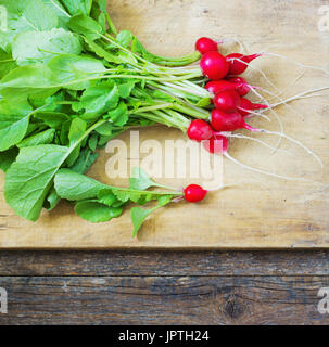 Fresche ravanelli su un tagliere di legno, oltre adark tavolo in legno Foto Stock