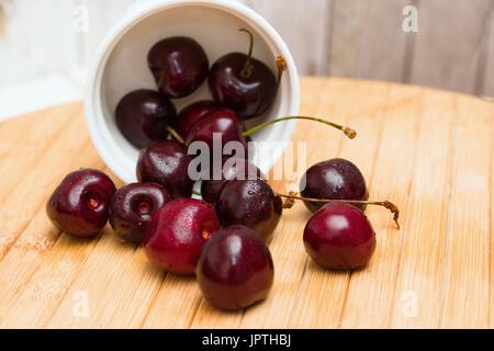 Ciotola di mature amarene versato su scheda in legno Foto Stock