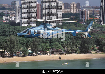 Bell 430 battenti lungo il tragitto su una spiaggia di sabbia e alberi verdi con grattacieli dietro Foto Stock