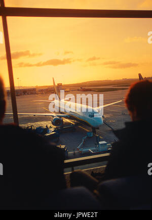 I passeggeri in attesa di una piena partenza-lounge accanto a Windows con un Ryanair Boeing 737-800 parcheggiata fuori al tramonto Foto Stock