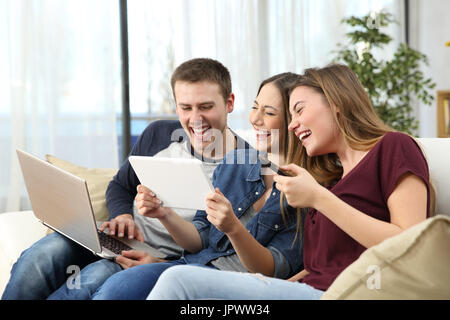 Tre amici felici di ridere hard guardare video seduto su un divano a casa Foto Stock