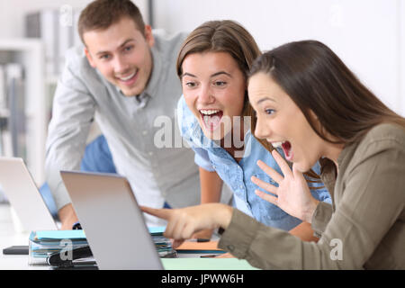 Tre dipendenti eccitati ricevendo buone notizie on line in ufficio Foto Stock