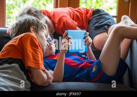 Young Boy giocare giochi per computer su iPad con altri ragazzi a guardare, primo piano Foto Stock