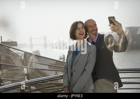Entusiasta, sorridente azienda giovane tenendo selfie con la fotocamera del telefono sul soleggiato ponte urbano, London, Regno Unito Foto Stock