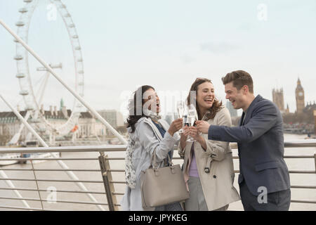 Entusiasta, sorridente amici celebrando, tostatura champagne sul ponte urbano vicino al Millennium Wheel, London, Regno Unito Foto Stock