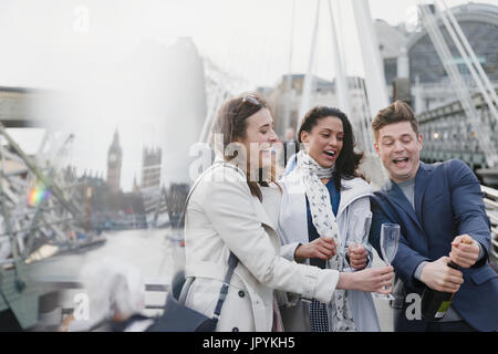 Gli amici di popping champagne, celebrando sul ponte urbano, London, Regno Unito Foto Stock