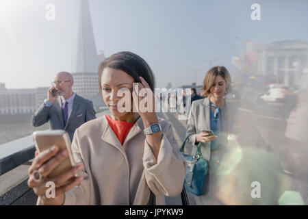 Imprenditrice tramite telefono cellulare di sunny urbano ponte pedonale, London, Regno Unito Foto Stock