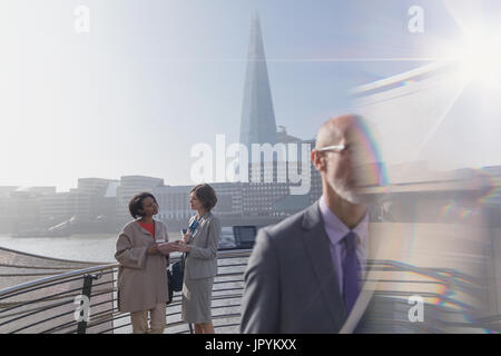 Imprenditrici con tavoletta digitale parlando sulla soleggiata ponte urbano, London, Regno Unito Foto Stock