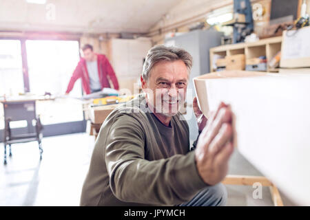 Sorridente falegname maschio esaminando barca di legno in officina Foto Stock