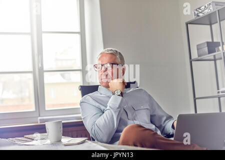 Fiducioso, pensieroso uomo d affari con computer portatile che guarda lontano in office Foto Stock
