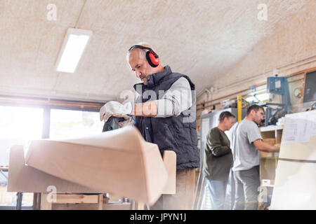 Senior falegname utilizzando sander, la levigatura del legno barca in officina Foto Stock