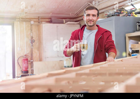 Ritratto fiducioso falegname maschio bere il tè in barca di legno in officina Foto Stock