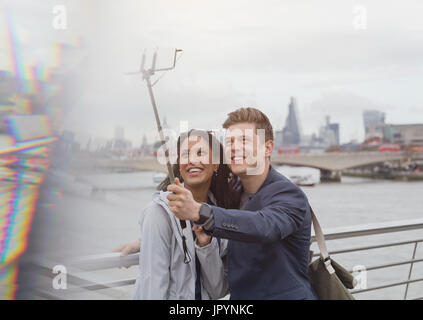 Giovane turista tenendo selfie con la fotocamera del telefono selfie stick al Tamigi waterfront, London, Regno Unito Foto Stock
