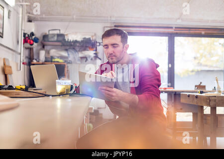 Falegname maschio utilizzando digitale compressa, bere il tè al banco di lavoro in officina Foto Stock