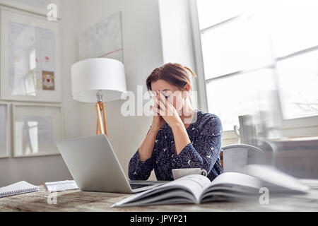 Stanco, ha sottolineato imprenditrice a notebook con testa in mani Foto Stock