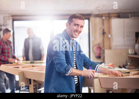 Ritratto sorridente falegname maschio di legno di misura sulla barca in officina Foto Stock