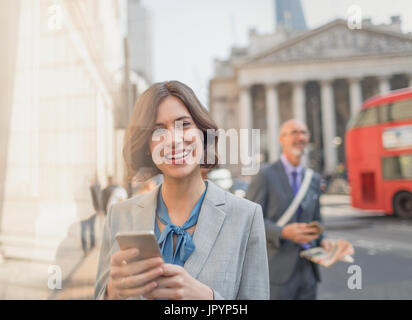 Ritratto sorridente imprenditrice texting con telefono cellulare sulla città urbana Street, Londra, Regno Unito Foto Stock
