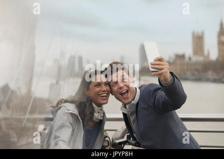 Giocoso giovane turista tenendo selfie con la fotocamera del telefono sul ponte di Londra, Regno Unito Foto Stock