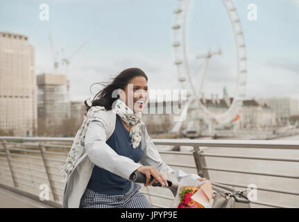 Entusiasta, Donna sorridente in bicicletta sul ponte in prossimità di Millennium Wheel, London, Regno Unito Foto Stock