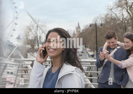 Donna sorridente parlando al cellulare sul ponte urbano, London, Regno Unito Foto Stock
