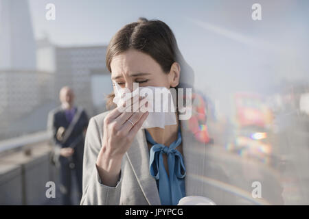 Imprenditrice con allergie soffia il naso nel tessuto sulla soleggiata marciapiede urbano Foto Stock