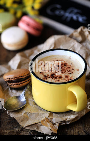 Buona mattina con cappuccino schiumoso in giallo vintage cup e amaretti Foto Stock