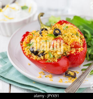 Couscous vegetariano pepe farcito con insalata di rucola e salsa di yogurt bianco su uno sfondo di legno Foto Stock