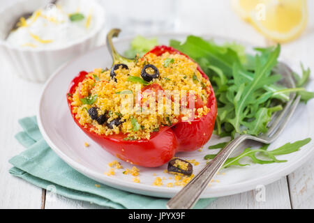 Couscous vegetariano pepe farcito con insalata di rucola e salsa di yogurt bianco su uno sfondo di legno Foto Stock