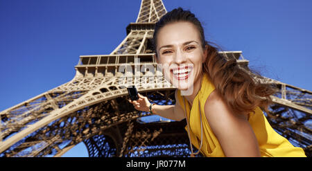 Turistica, senza dubbio, ma ancora in modo divertente. Ritratto di sorridente giovane donna prendendo foto con una fotocamera digitale contro la Torre Eiffel a Parigi, Francia Foto Stock