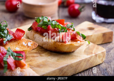 Pomodoro e Basilico bruschetta con crostini di pane all'aglio, Italiano tradizionale di antipasto rustico tagliere di legno Foto Stock