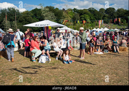Famiglie godere il sole seduti a bere e mangiare fuori tende e tabelloni elettronici al porto Eliot Festival Cornwall Regno Unito Foto Stock