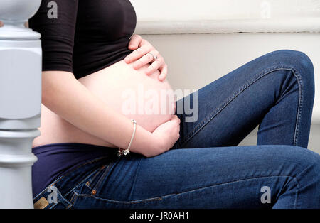 adolescente incinta seduto sulle scale in casa Foto Stock