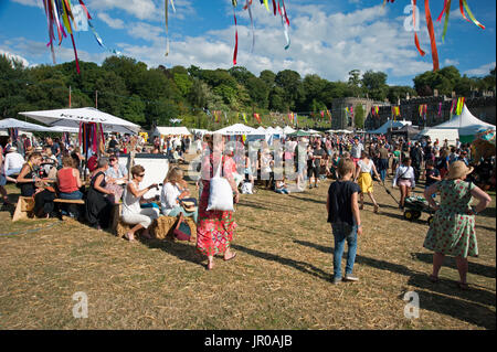 Famiglie godere il sole seduti a bere e mangiare fuori tende e tabelloni elettronici al porto Eliot Festival Cornwall Regno Unito Foto Stock