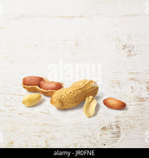 Un guscio di arachidi aperto a metà e noccioline su un dipinto di bianco superficie in legno Foto Stock