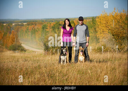 Ritratto di un giovane in piedi con i loro due cani e un autunno paesaggio colorato in background; Alberta, Canada Foto Stock