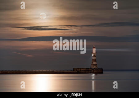 Roker faro incandescente alla fine di un molo sotto una luminosa Luna Piena riflettendo sulla tranquilla acqua; Sunderland, Tyne and Wear, Inghilterra Foto Stock