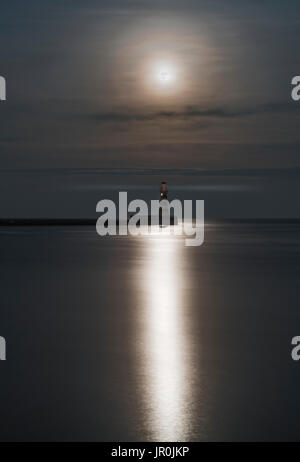 Roker Faro all'estremità di un molo sotto una luminosa Luna Piena riflettendo sulla tranquilla acqua; Sunderland, Tyne and Wear, Inghilterra Foto Stock