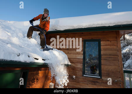 Una giovane donna rimuove la neve dal tetto della sua casa; Omero, Alaska, Stati Uniti d'America Foto Stock