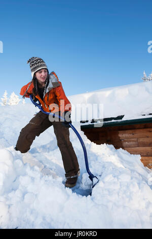 Una giovane donna rimuove la neve dal tetto della sua casa; Omero, Alaska, Stati Uniti d'America Foto Stock