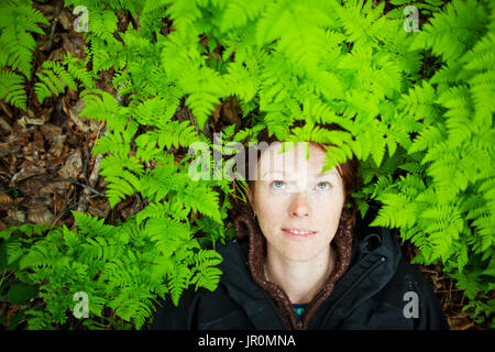 Una donna getta la sua testa sul suolo della foresta tra il verde brillante, lussureggianti felci; Alaska, Stati Uniti d'America Foto Stock