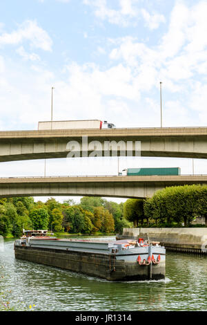 Un vuoto che la bettolina scendendo lungo il corso del fiume Marne verso Parigi mentre semirimorchi camion guidare sulle rampe della A86 autostrada su vie navigabili. Foto Stock