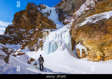 Un backcountry rider osserva una cascata ghiacciata lungo un miglio Creek in Alaska Range. Foto Stock